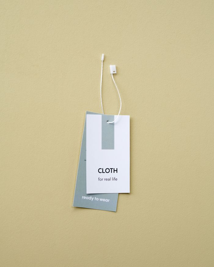 Close-up of minimalist clothing labels against a beige backdrop, featuring 'CLOTH for real life'.